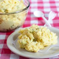 A plate of classic potato salad on a picnic table with plastic cutlery.