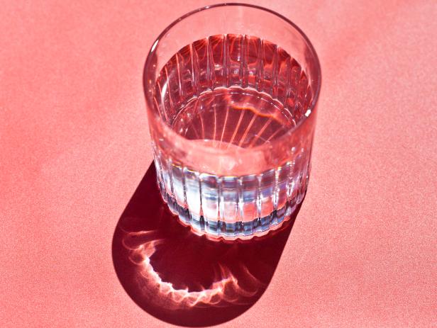 Close-up of a glass of water shining in the sunlight on a pink background.