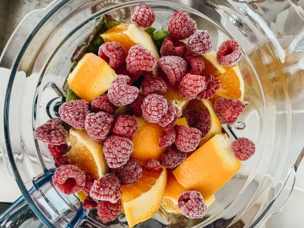 Vegetables topped with oranges and frozen raspberries before blending into a smoothie.