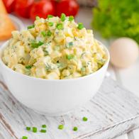 Egg salad with chopped green onions on top in a white bowl for cooking a sandwich on a white wooden background. Selective focus.