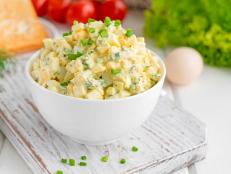 Egg salad with chopped green onions on top in a white bowl for cooking a sandwich on a white wooden background. Selective focus.