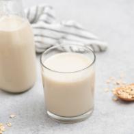 Vegan oat milk in glass on grey concrete table background. Non dairy milk alternative