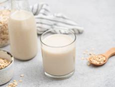 Vegan oat milk in glass on grey concrete table background. Non dairy milk alternative