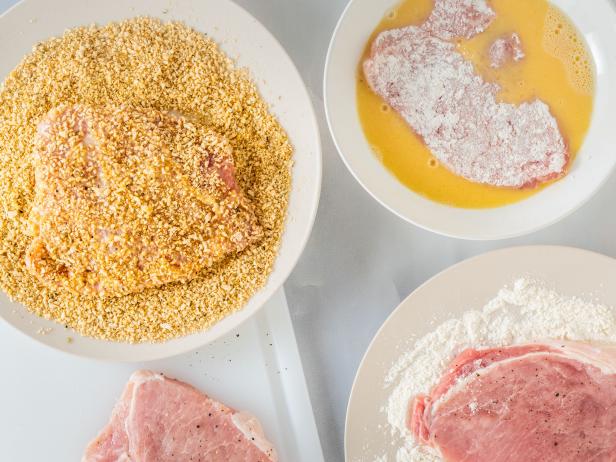 Breaded pork chops recipe. Pork chops on a plate with flour, eggs, and bread crumbs, close up view from above