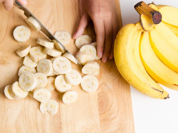 Woman slice ripe banana on wooden board for cooking or processing in the kitchen