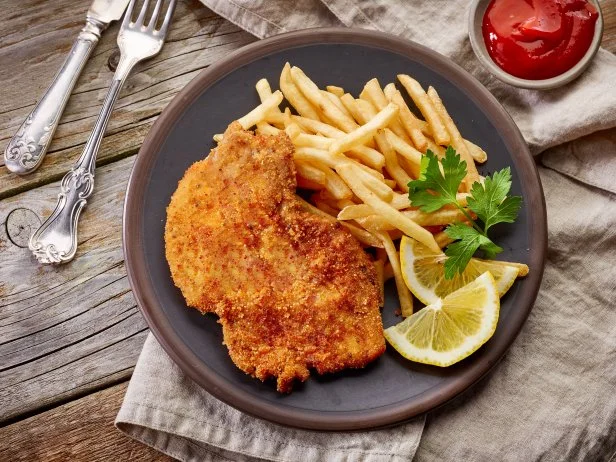 schnitzel and fried potatoes on dark plate, top view