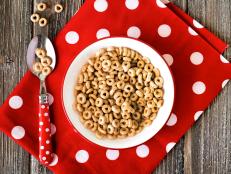 A bowl of cereal and a red polka dot napkin on a wooden table.