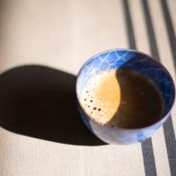 Sunny table with a porcelain coffee cup with fresh coffee, with a crisp dark shadow.