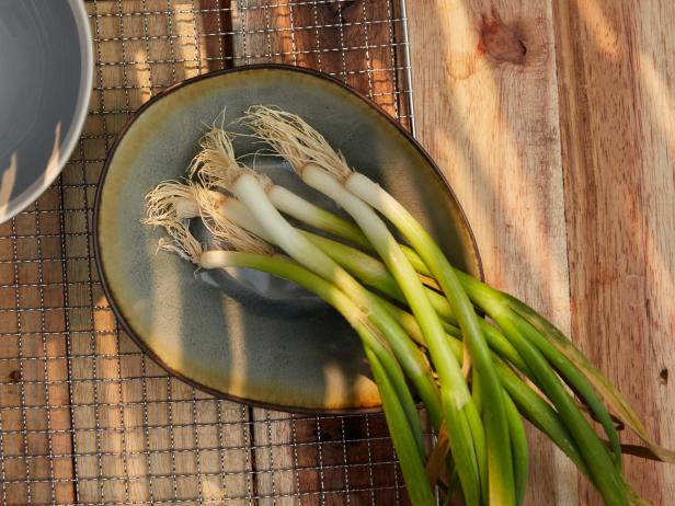 Cleaning scallions preparation. Washed spring onion in decorative crockery. Empty bowl. Stainless stel grid on wooden plank. High point of view. Light effect.