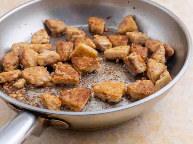 Cut tempeh pieces pan-fried in olive oil. Yellowish decorative background.