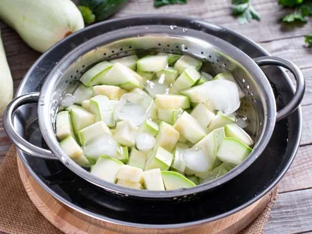 Boiled vegetables, zucchini in a colander in ice water after blanching. Frozen Food Concept.