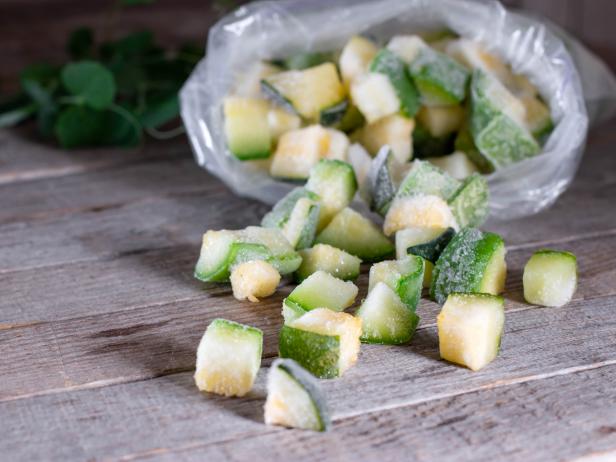 Frozen cubes of zucchini in a plastic bag on the old wooden background