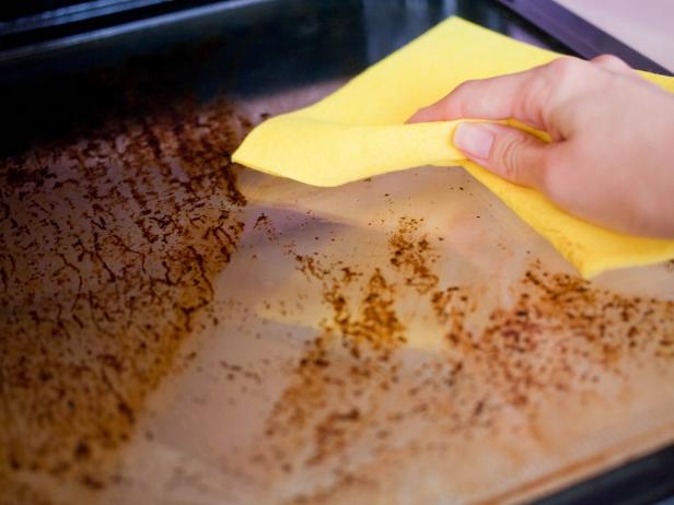 A female hand is holding a yellow rag and washing the dirty door of the oven.