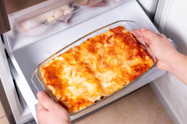 Frozen ready meals. Man's hands are taking frozen lasagna from the freezer of the fridge. Concept of ready made frozen dishes and saving time on cooking food.