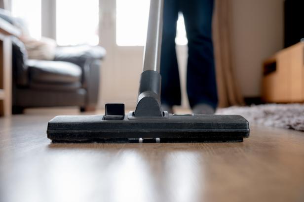 A woman using a cylinder vacuum cleaner on a laminate floor.