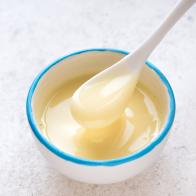Condensed milk pouring in white bowl. Sweet vanilla sauce, condensed or evaporated milk, top view, copy space.