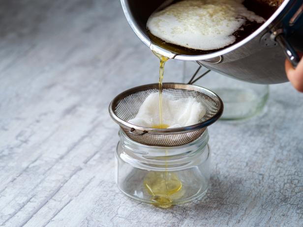 The oil is filtered into a glass jar through a metal sieve and cheesecloth.
