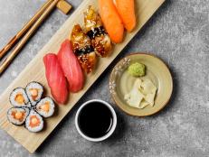 Variety of sushi on a tray with chopsticks and soy sauce on stone background