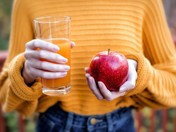 A young woman in a yellow sweater holding a glass of apple juice and a fresh apple.