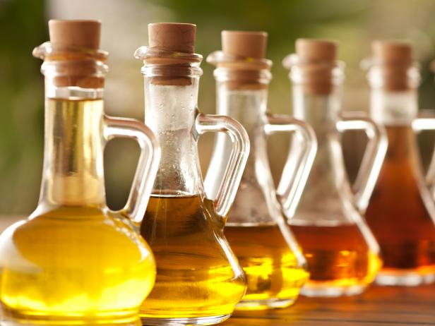 various colours of olive oil and vinegar in glass bottles aligned on a wooden table at Mediterranean sea