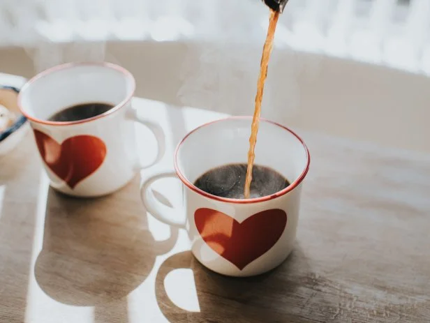 Pouring black coffee into coffee cups with heart design. Space for copy. Conceptual.