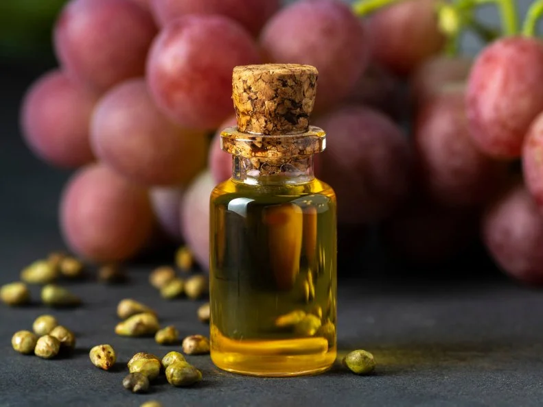 Grape seed oil in a glass jar and fresh grapes