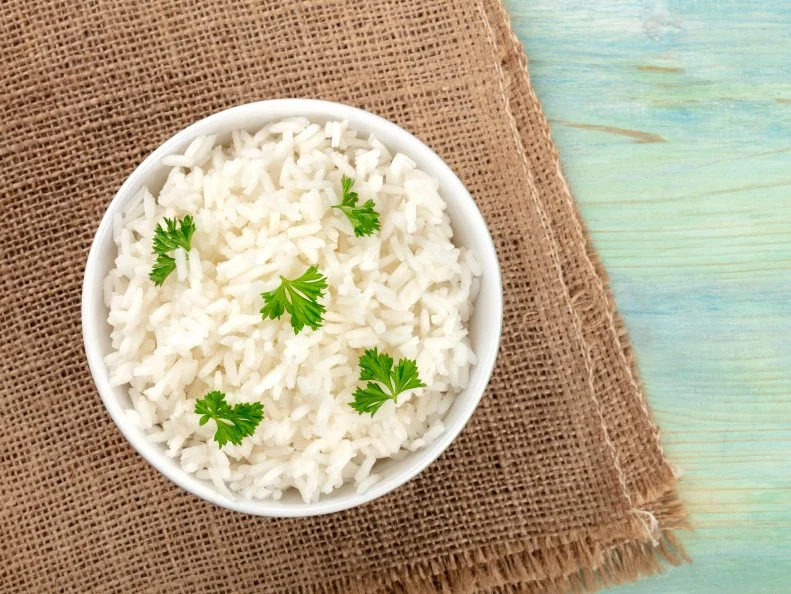 A photo of a bowl of cooked white long rice, shot from the top on rustic textures with copy space