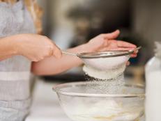 Cropped shot of a woman sifting flour into a glass bowl