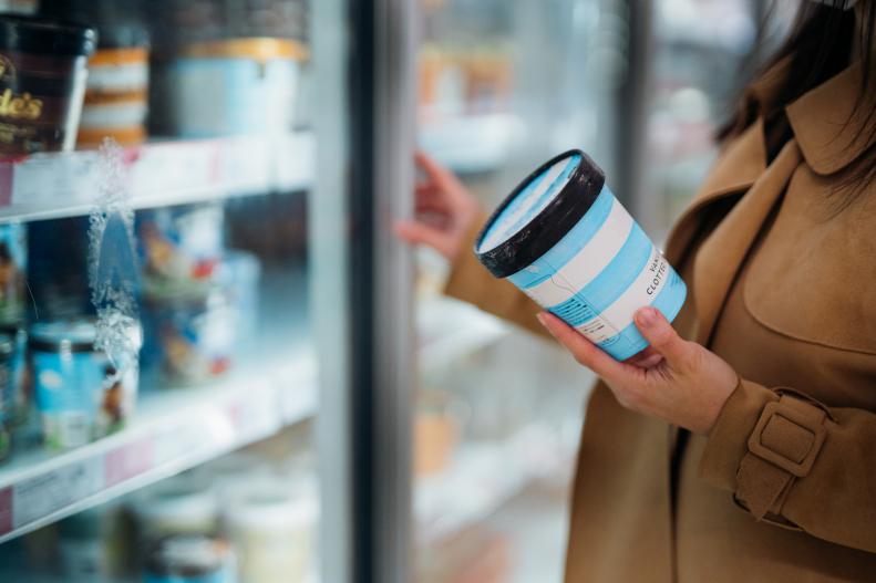 Close up shot of woman holding a cup of protein ice cream in supermarket. Grocery shopping in supermarket.