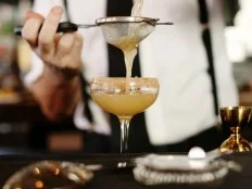 A bartender pours a freshly made drink into a glass.