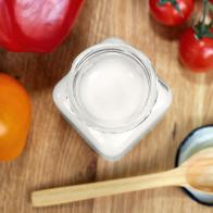 Coconut oil in a glass jar. Near the jar are sweet peppers, tomatoes and a wooden spoon. Healthy food concept. Flat lay