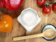Coconut oil in a glass jar. Near the jar are sweet peppers, tomatoes and a wooden spoon. Healthy food concept. Flat lay