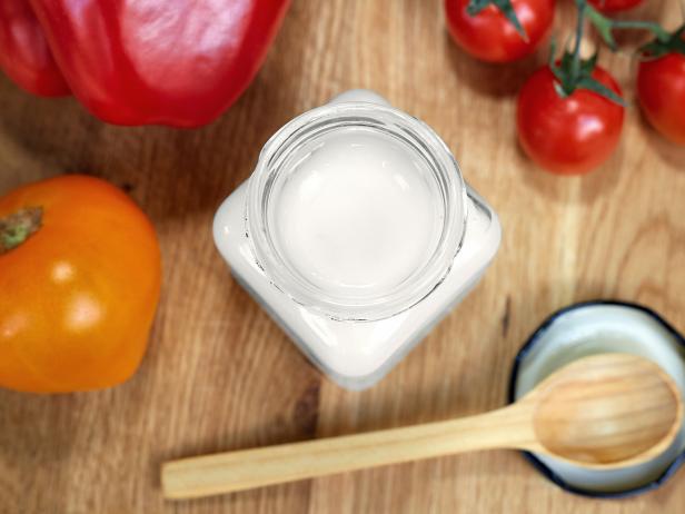Coconut oil in a glass jar. Near the jar are sweet peppers, tomatoes and a wooden spoon. Healthy food concept. Flat lay