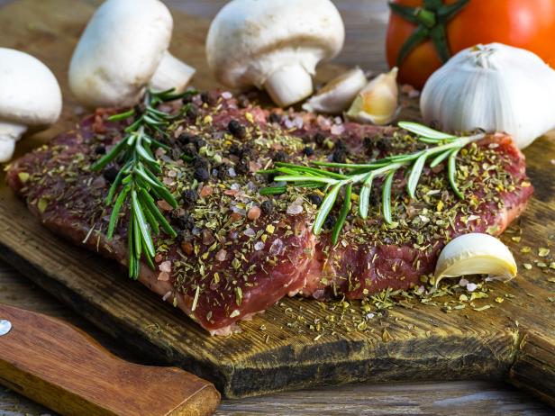 Raw beef steak served with vegetables and herbs on rustic wooden board background. Close up. Selective focus. Copy space