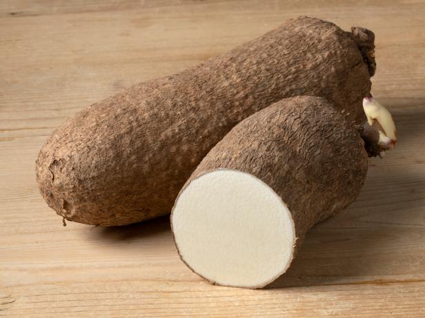 Whole and halved raw African yam on wooden background close up