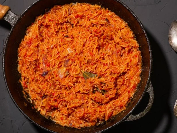 Jollof rice in a frying pan on a dark background. A traditional Nigerian dish of rice, tomatoes and spices.