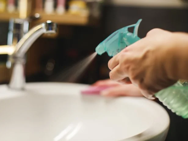 Woman in quarantine during coronavirus pandemic doing chores cleaning bathroom with natural mixture of vinegar, water and essential oil.
