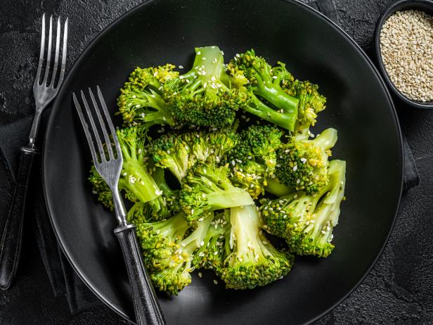 Boiled broccoli with spices in a plate. Black background. Top view.