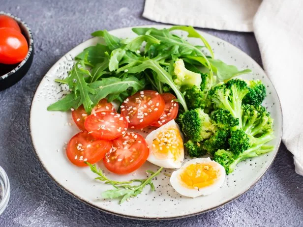 A plate with broccoli, arugula, tomato and boiled egg on a plate on the table. Ketogenic diet. Close-up