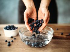 Unrecognizable woman cleaning blueberries in bowl with water on kitchen counter