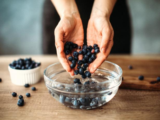 Unrecognizable woman cleaning blueberries in bowl with water on kitchen counter