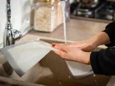 Female hands cleaning a silicone baking mat in cold water from a faucet after cooking. Selective soft focus