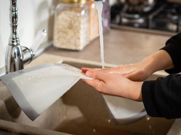 Female hands cleaning a silicone baking mat in cold water from a faucet after cooking. Selective soft focus