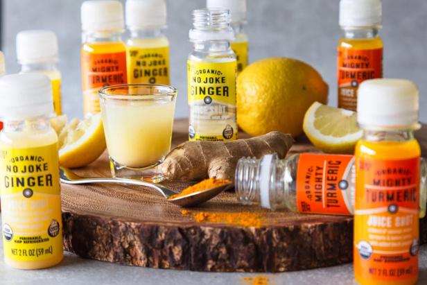 Trader Joe's Organic No Joke Ginger and Mighty Turmeric Juice Shots, on wood board, one pored in a shot glass, and ginger chunk and turmeric powder on surface