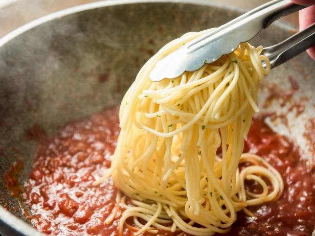 Cooked Italian spaghetti being put in the pan with hot bolognese sauce