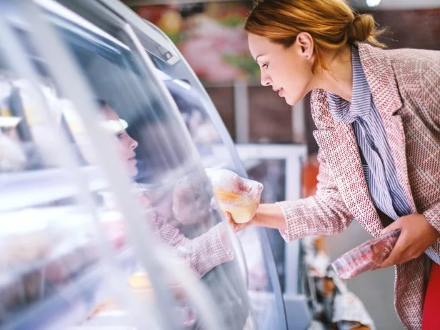 Attractive smiling brunette taking meat from a fridge at local supermarket. Side view. Horizontal.