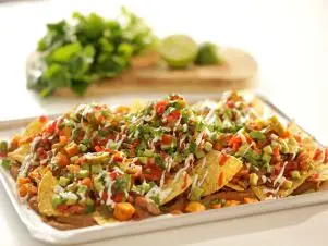 Horizontal clsoe up, side-on plate of nachos, board with greens in background, as seen on Mary McCartney Serves It Up, season 3.