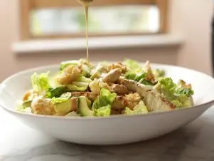 Landscape, side on close-up of Caesar salad with dressing being poured overtop, as seen on Mary McCartney Serves It Up, season 3.