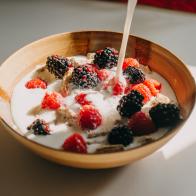 Dairy free milk pouring into a bowl of whole grain cereal, raspberries and blackberries.