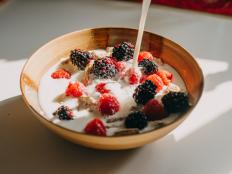 Dairy free milk pouring into a bowl of whole grain cereal, raspberries and blackberries.
